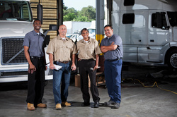 Image of four long haul truckers and their trucks in the maintenance facility