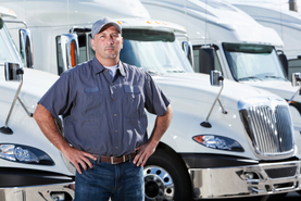 Image of long haul trucker in front of trucks in a parking lot